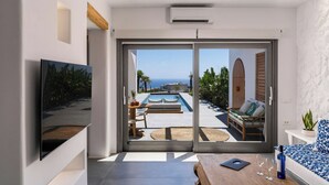 A modern room with a large sliding glass door leading to a pool area with a view of the sea. -  Numa Santorini (Santorini)