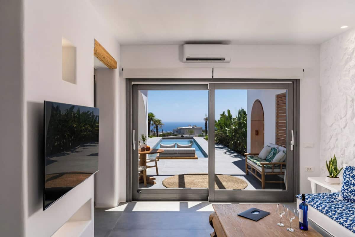 A modern room with a large sliding glass door leading to a pool area with a view of the sea.