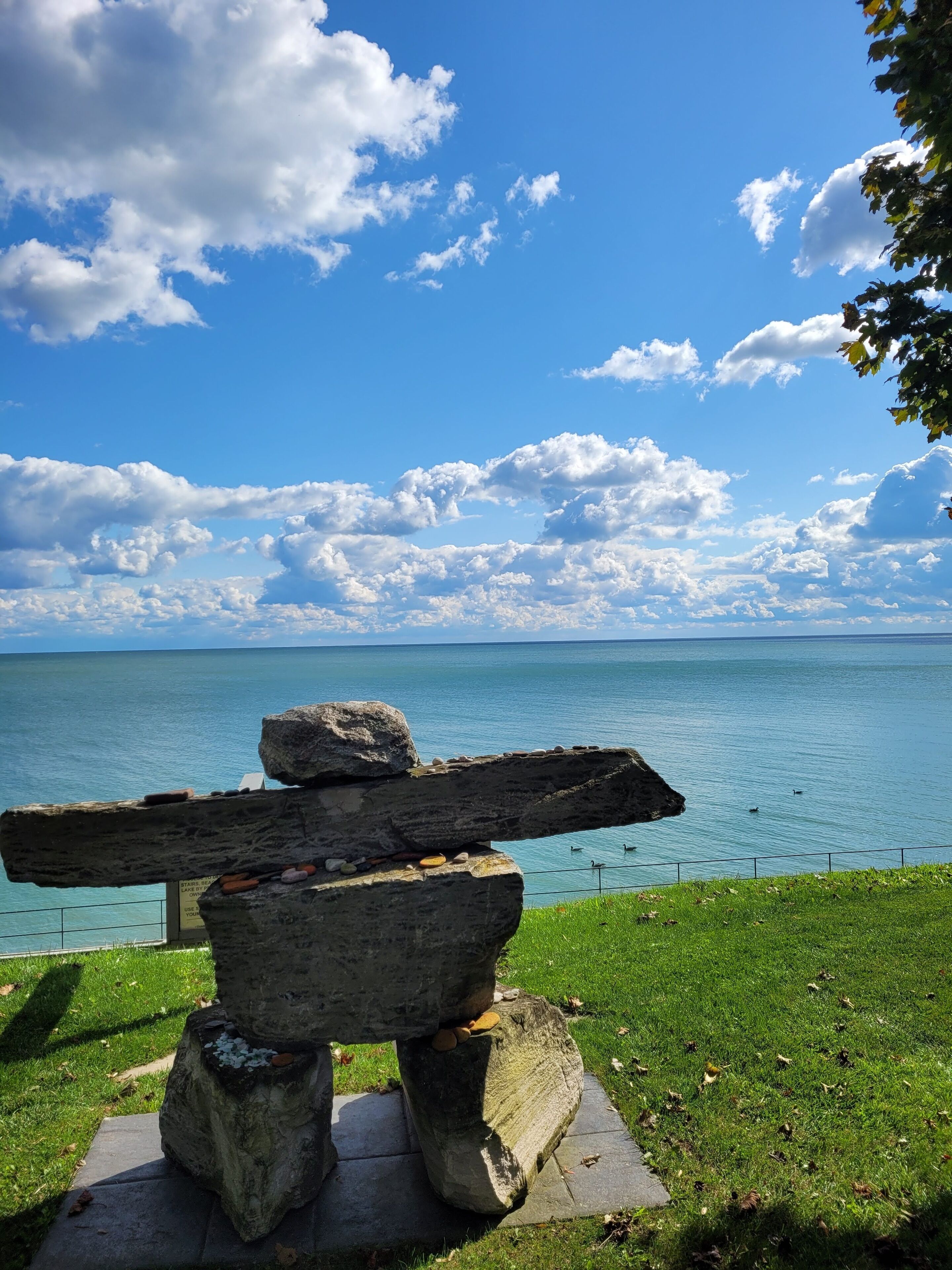 A stone structure with a wooden beam, set against a backdrop of a clear blue sky and calm sea.
