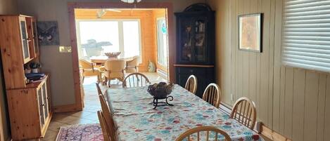 A dining area with a table set for four, surrounded by wooden chairs, a patterned rug, and a ceiling fan.