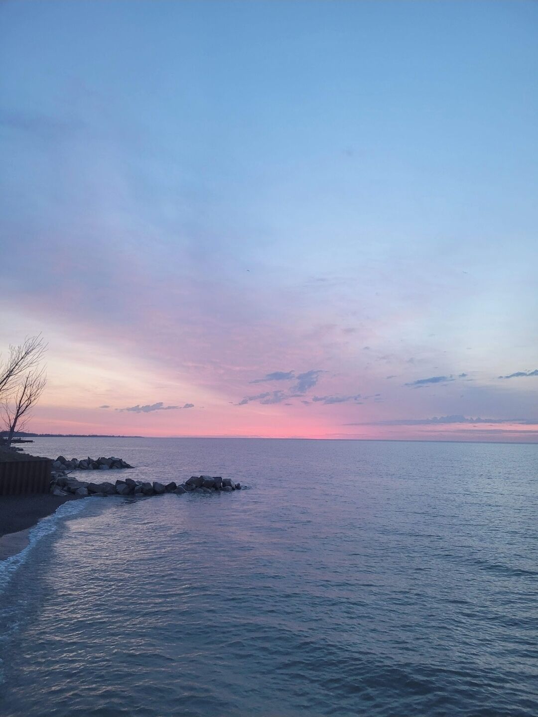 Un paisaje costero con mar en calma, un litoral rocoso y cielo despejado.