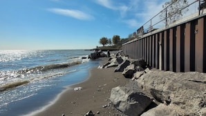 Une plage bordée d’une côte rocheuse, avec une rambarde en métal et un ciel dégagé.