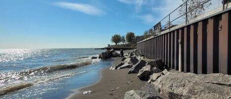 A beach with a rocky shoreline, a metal railing, and a clear sky.