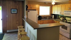 Une cuisine avec des meubles de rangement en bois, un réfrigérateur, une cuisinière et une fenêtre.