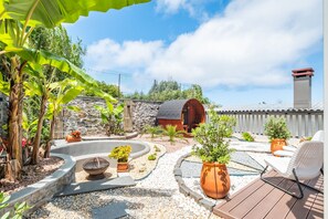 Un espace patio agrémenté d’un mur en pierre, d’une barrique en bois, d’un foyer et de plantes en pot.