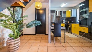 A modern kitchen with yellow cabinets, stainless steel appliances, and a dining area with a chair and table. - Ocean Panorama House by Madeira Sun Travel (Calheta)