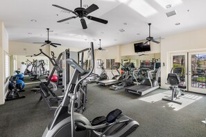 Uma academia com ventiladores de teto, equipamentos de exercícios e um espelho grande.