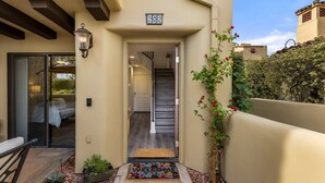 Une entrée d’immeuble avec un paillasson, une plaque de numéro, un escalier et un pot de fleurs.