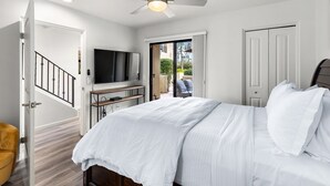 Une chambre à coucher comprenant un lit, un ventilateur de plafond, une télévision et une porte donnant sur un balcon.