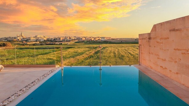 A rooftop infinity pool with a view of a cityscape and fields during sunset. - Sunset Serenity - Four Bedroom Villa, Sleeps 8 (San Lawrenz)