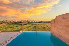 Ein Infinity-Pool auf dem Dach mit Blick auf eine Stadtlandschaft und Felder bei Sonnenuntergang.