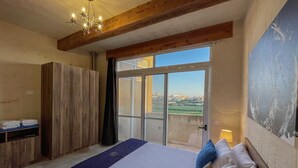 A bedroom with a large bed, wooden wardrobe, and a view through a glass door. - Sunset Serenity - Four Bedroom Villa, Sleeps 8 (San Lawrenz)