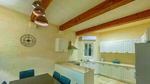 A compact kitchen with white cabinets, a central island, and a dining area with a table and chairs. - Sunset Serenity - Four Bedroom Villa, Sleeps 8 (San Lawrenz)
