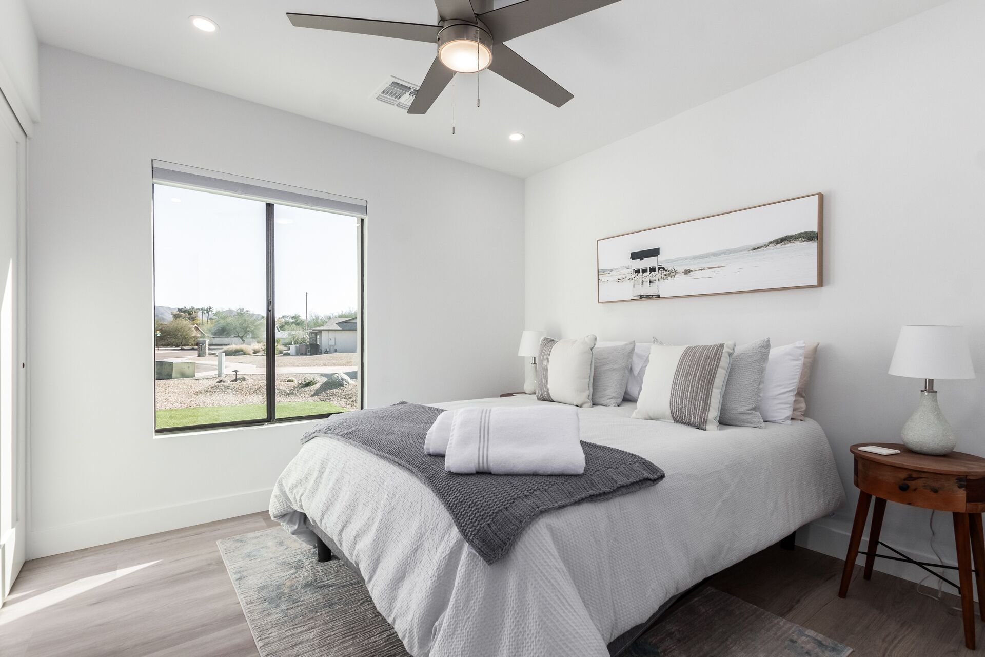 A modern bedroom with a large bed, a ceiling fan, a view of the outdoors, and a framed picture on the wall.