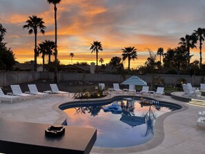 A pool area with lounge chairs and a small pool, surrounded by palm trees and a sunset view.