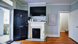 A hallway with a black door marked "1343", a fireplace, a mounted TV, and a framed map on the wall. - Charming and cozy home by a Historic District (Columbus)