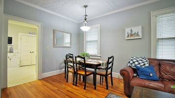 A dining area with a wooden table and chairs, a chandelier, and a brown leather couch with a blue pillow.