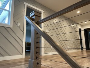 Eine moderne Treppe mit Holzwurf und Metallspindeln, die zu einem Raum mit geometrischem Wandmuster und Holzboden führt.