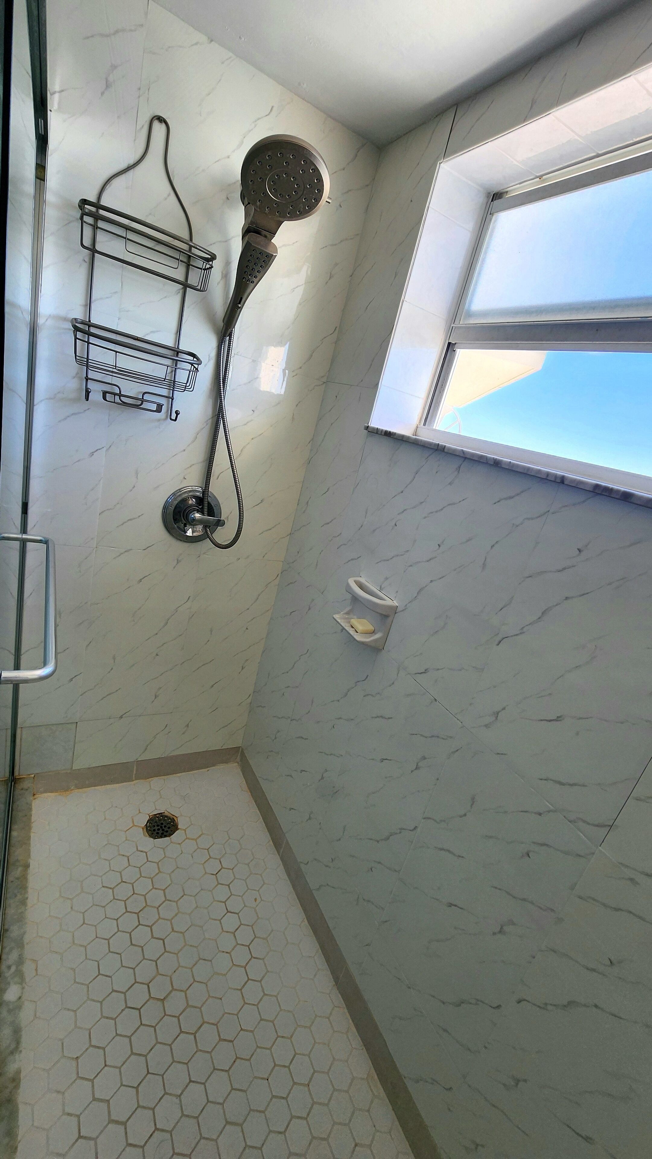 Een badkamer met een douche, toilet en raam.