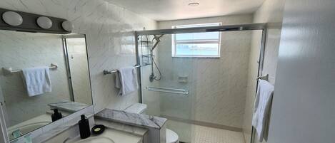 A modern bathroom with a glass-enclosed shower, a large mirror, a marble sink, and a toilet.