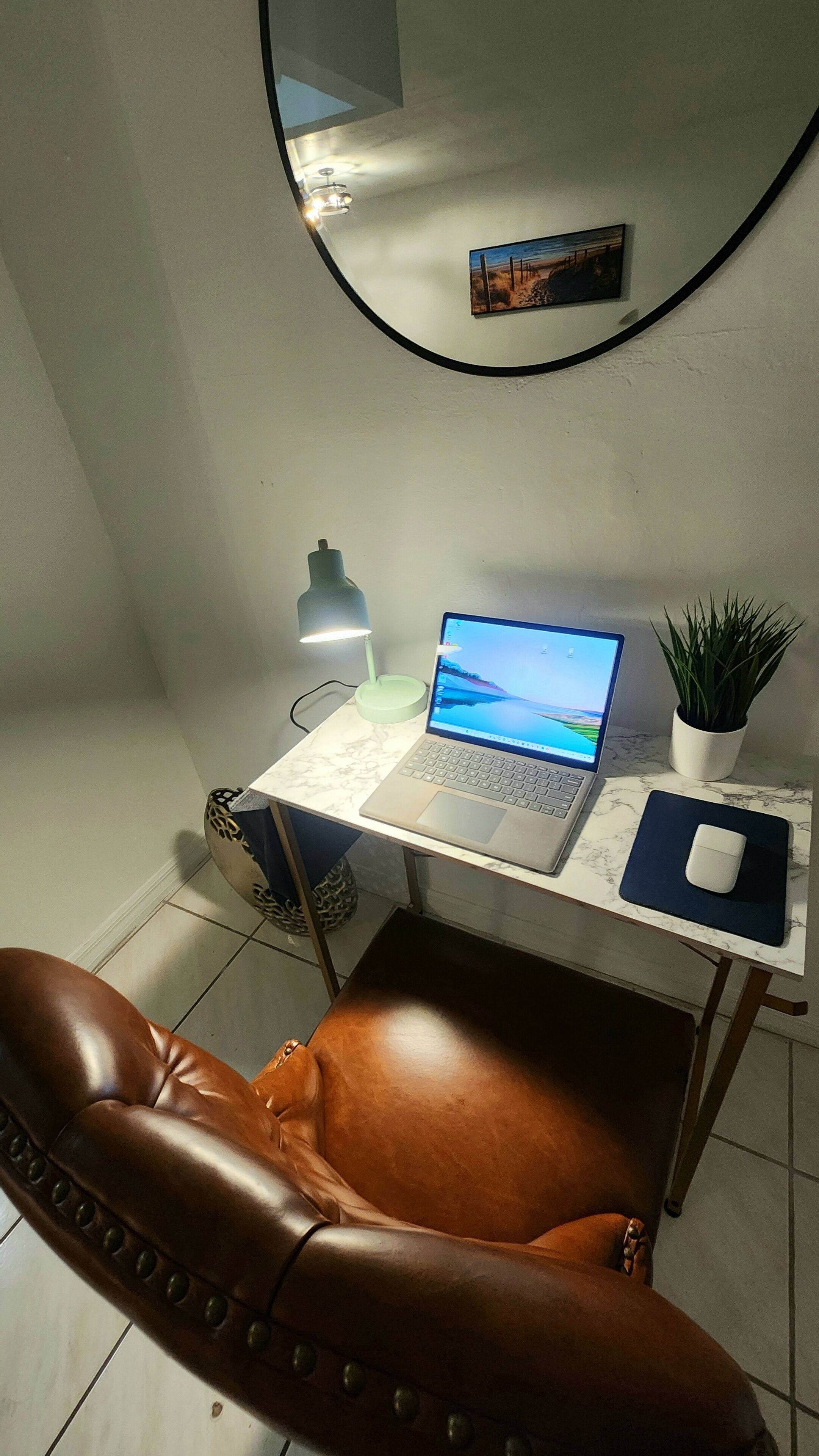 Un'area di lavoro con un portatile, una lampada da scrivania, una pianta in vaso e una poltrona in pelle.