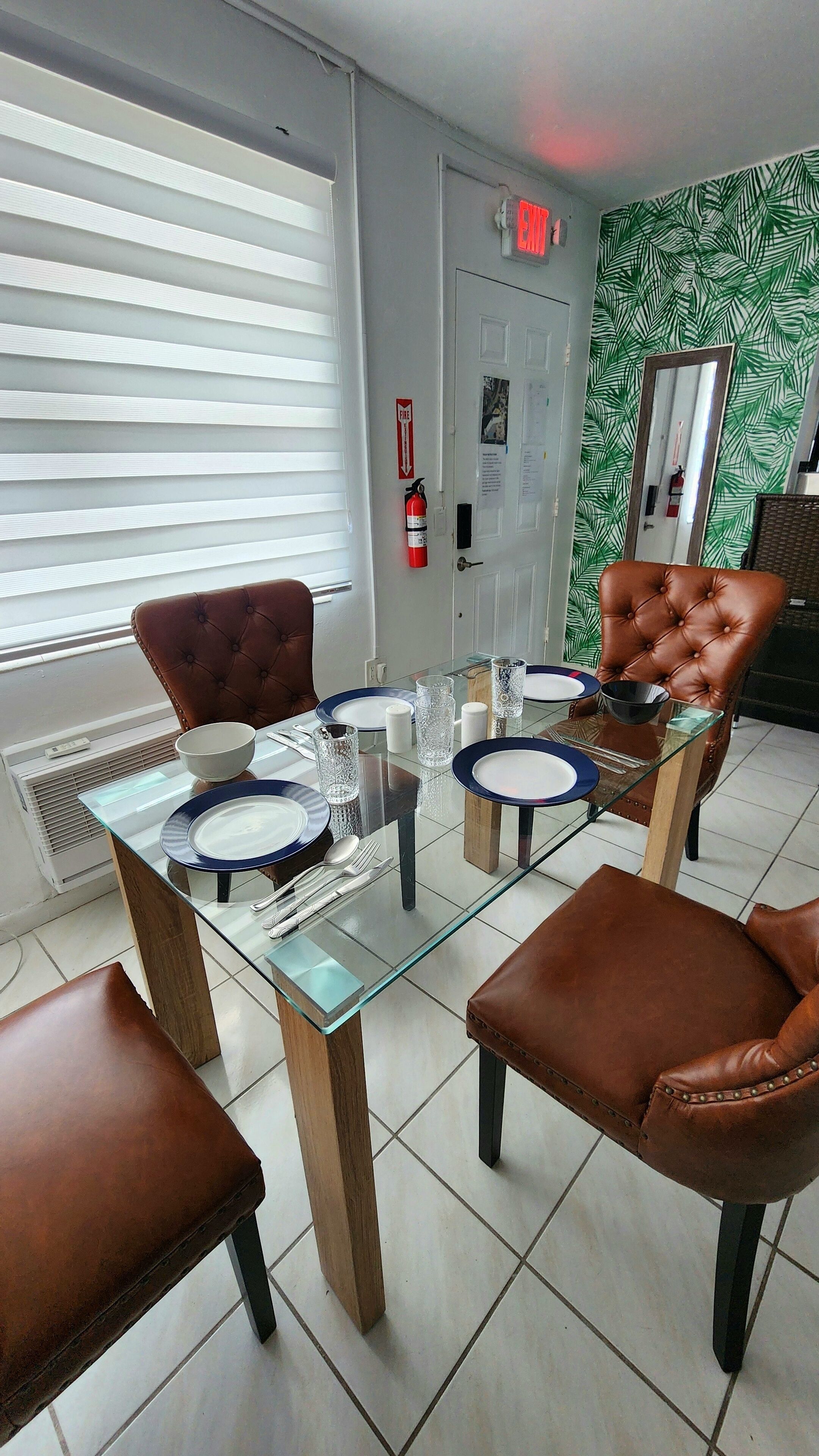 Een eetruimte met een glazen tafel, bruine lederen stoelen en een nooduitgangsbord.