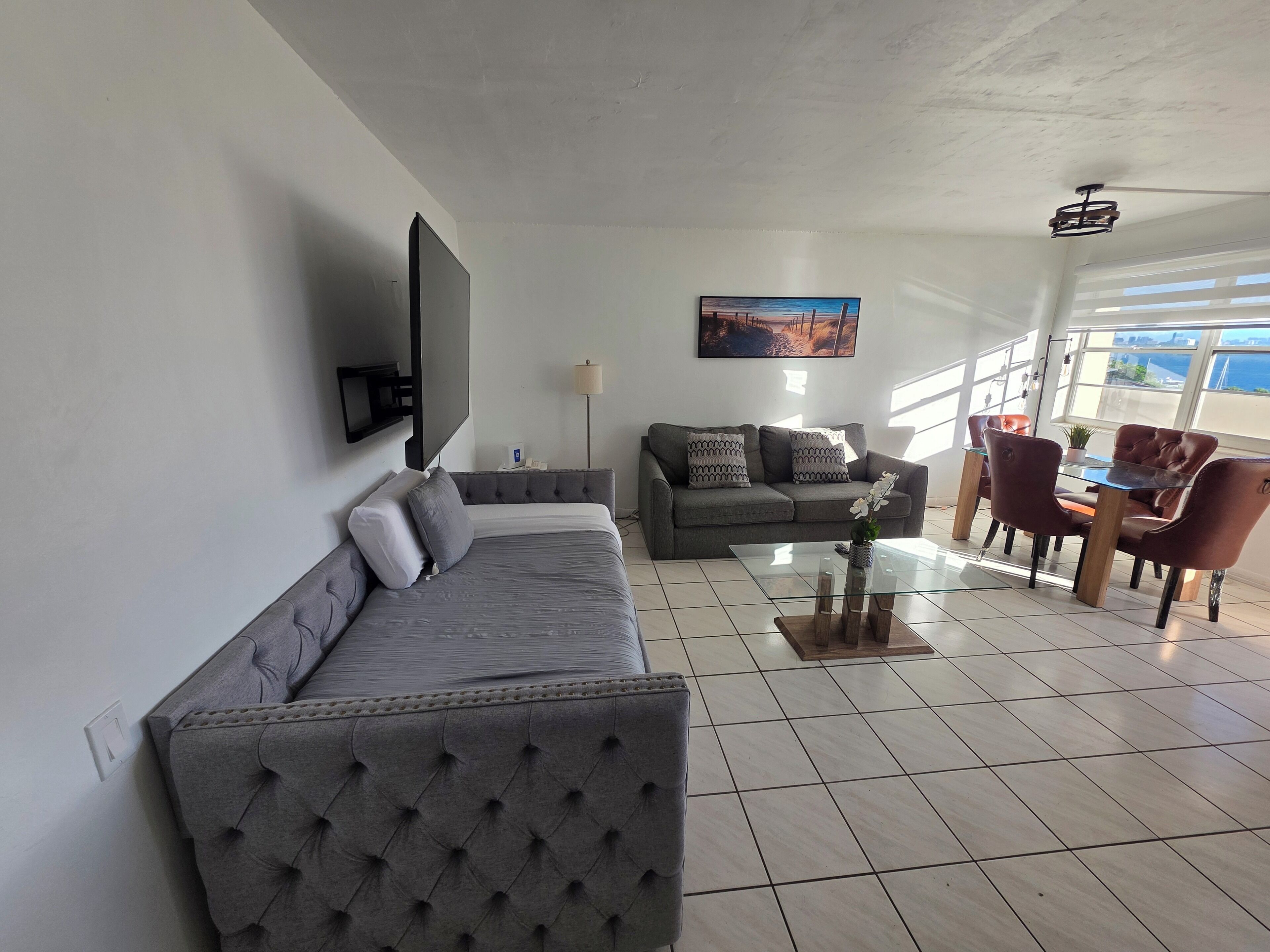 A modern living room with a grey sofa, a coffee table, and a dining area with chairs and a table.