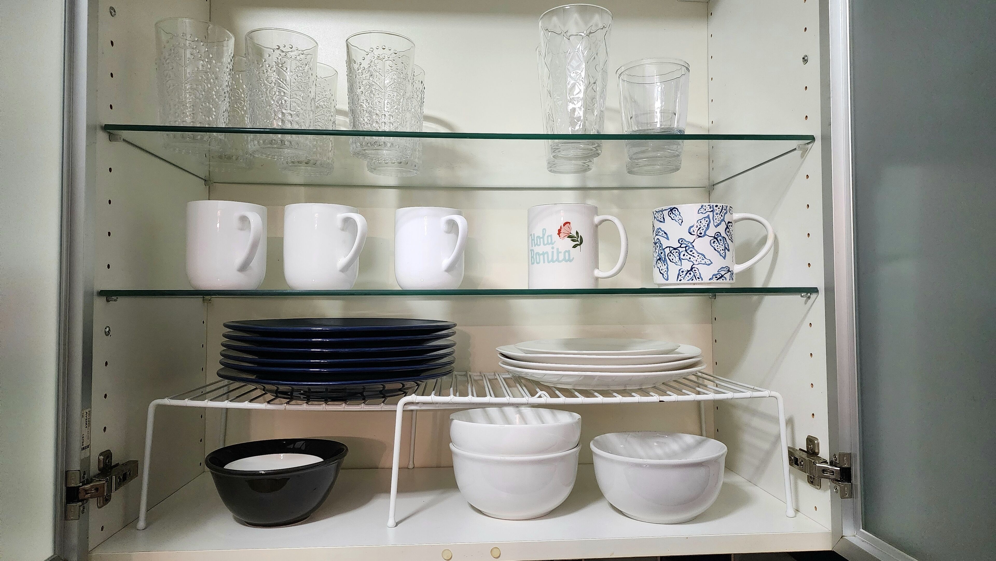 A kitchen cabinet with shelves holding various glassware, white mugs, and plates.
