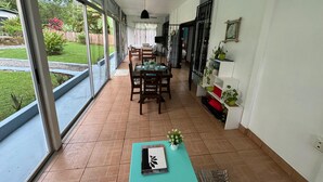 A spacious room with a dining area, large windows, and a view of a garden. - This house is a 2 bedroom(s), 2 bathrooms, located in Ojochal, Provincia de Puntarenas. (Ojochal)