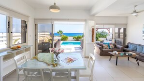 Een ruime woonkamer met een glazen tafel, witte stoelen, een bank en uitzicht op de oceaan.