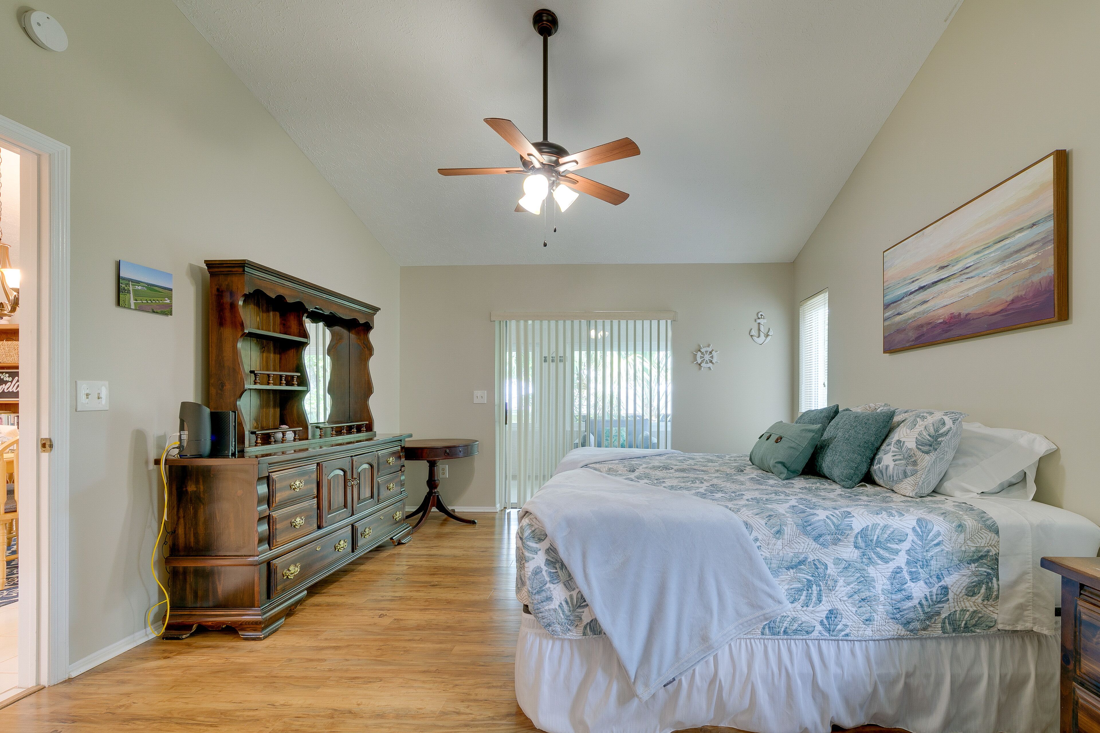 A bedroom with a bed, a ceiling fan, a dresser, and a window with blinds.