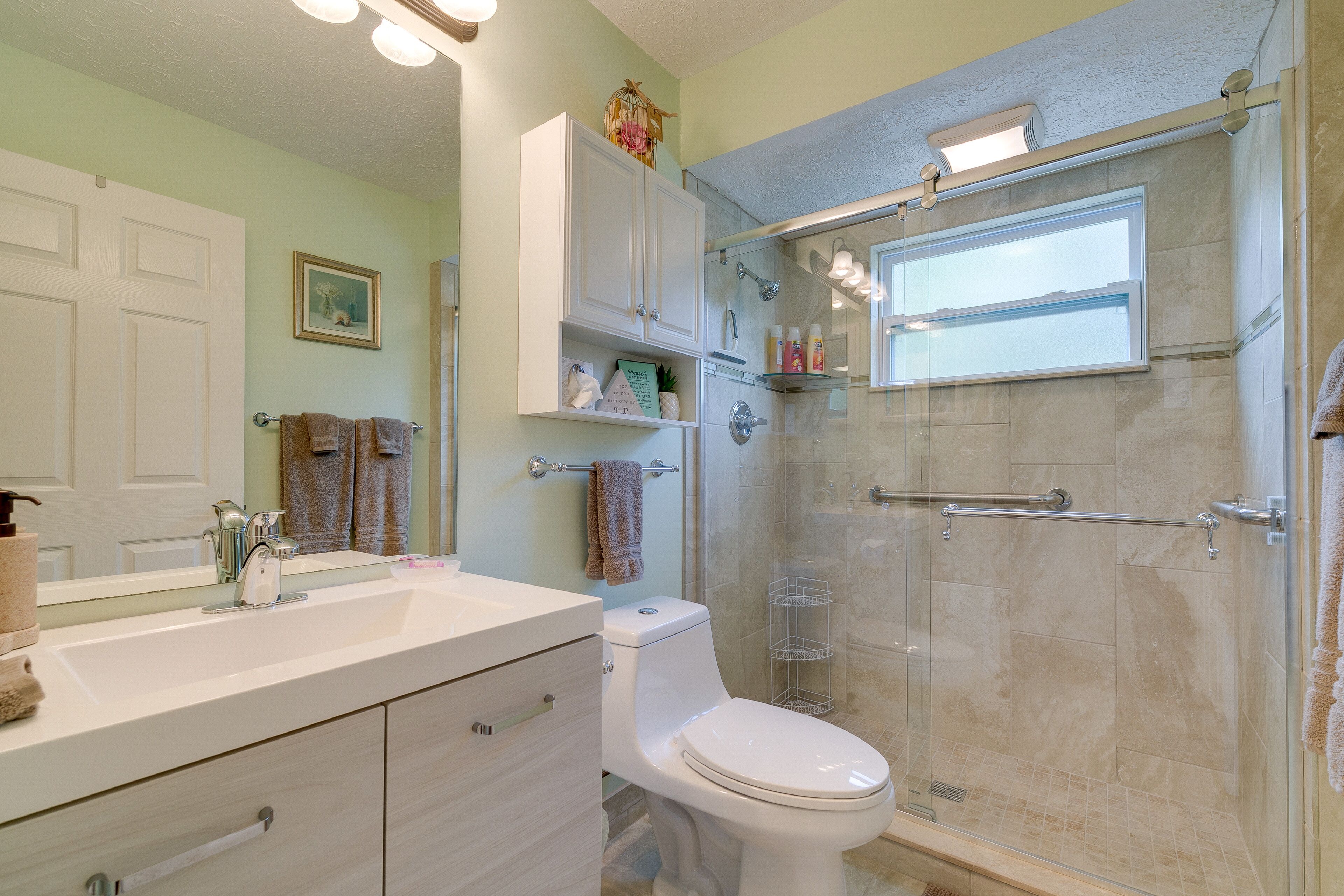 A bathroom with a white sink, a toilet, a glass shower enclosure, and a white cabinet above the sink.