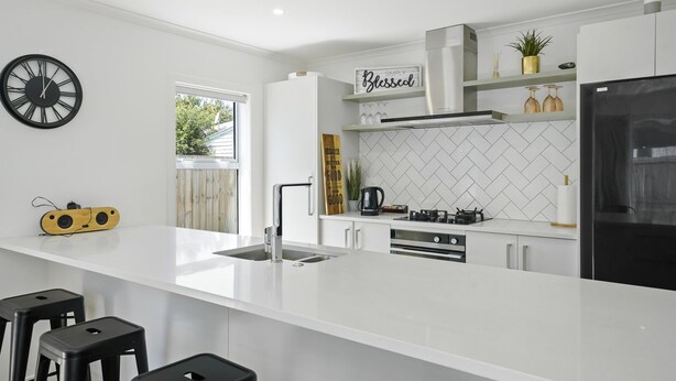 A modern kitchen with white cabinetry, a central island, a black refrigerator, and a herringbone tile backsplash. - Contemporary Comfort - Masterton Holiday Home (Masterton)
