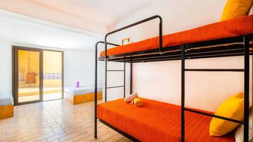 Une chambre avec des lits superposés, un plancher en bois, une porte-fenêtre coulissante donnant sur un espace extérieur et une petite table avec une chaise.