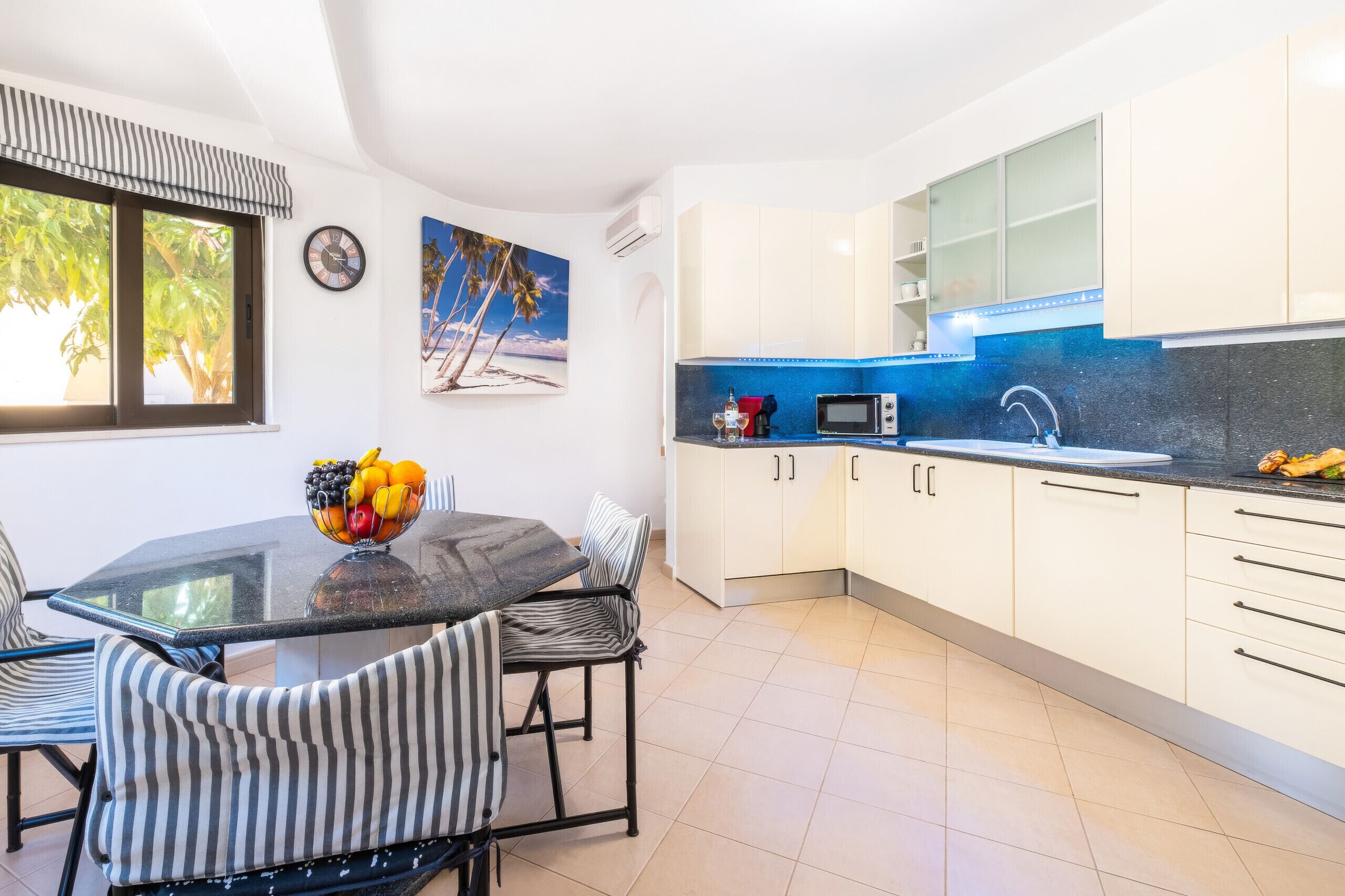 A modern kitchen with white cabinets, a blue backsplash, and a dining area with striped chairs.