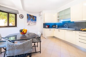A modern kitchen with white cabinets, a blue backsplash, and a dining area with a glass table and striped chairs. - Family retreat w/ pool & BBQ in Montechoro (Albufeira)