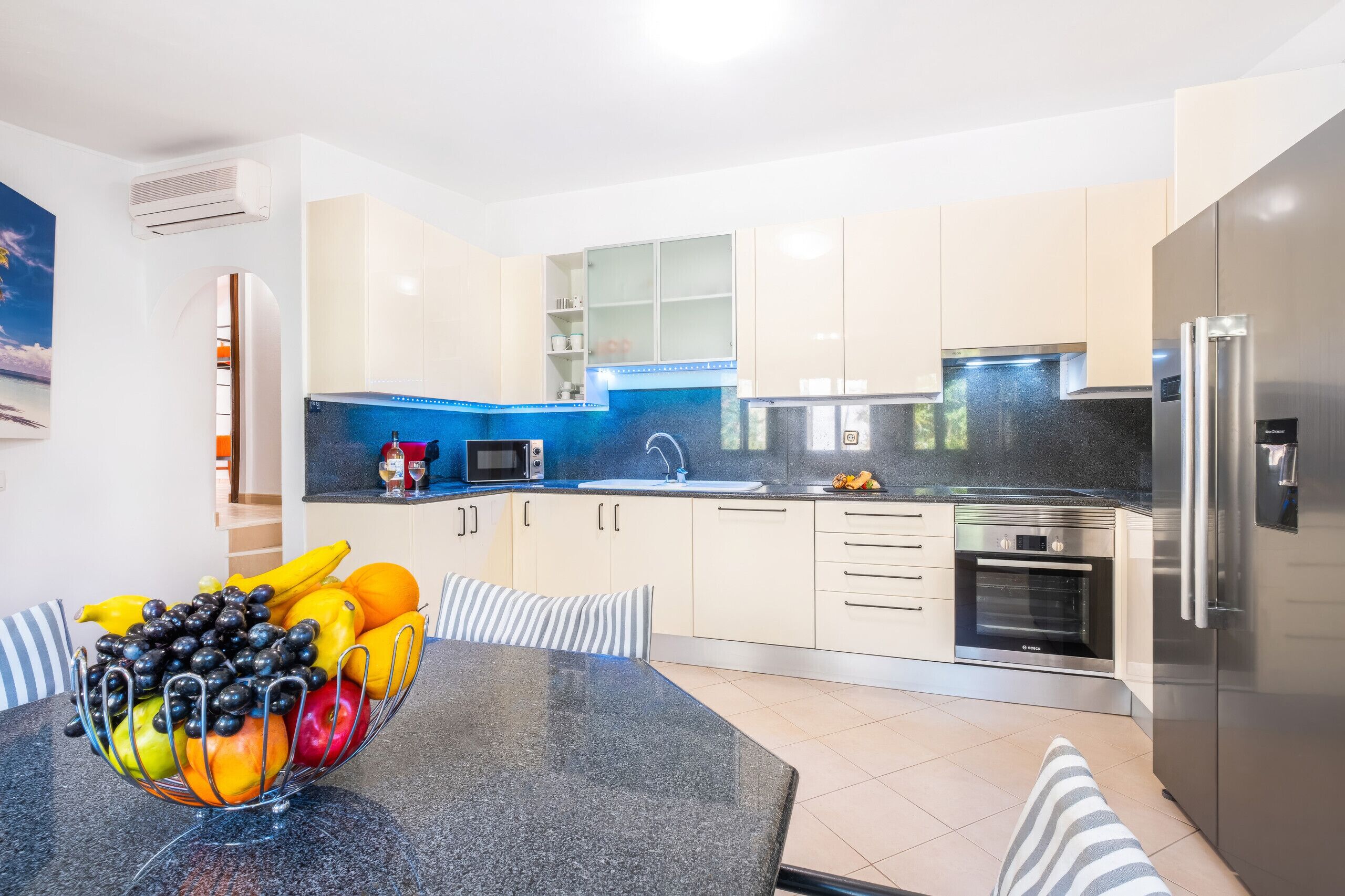 A modern kitchen with a granite countertop, stainless steel appliances, and a bowl of fruit on the table.