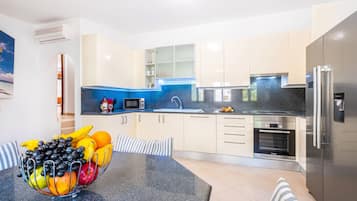 A modern kitchen with a granite countertop, stainless steel appliances, and a bowl of fruit on the table.