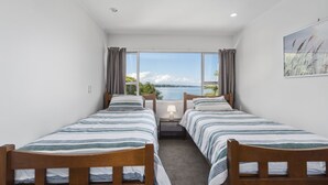 A room with two single beds, a large window with a view of the sea, and a painting on the wall. - Lakeside Terrace - Taupo Holiday Home (Taupo)