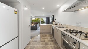 A modern kitchen with a gas stove, oven, and dishwasher, leading to a balcony with a sofa and dining table. - Lakeside Terrace - Taupo Holiday Home (Taupo)