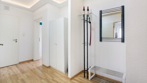 Un couloir avec un plancher en bois, des murs blancs, un radiateur et un miroir accroché au mur.