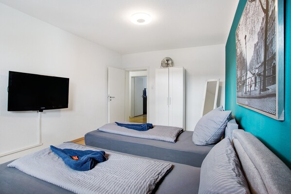 Une chambre avec deux lits, une télévision, une armoire et un tableau au mur.