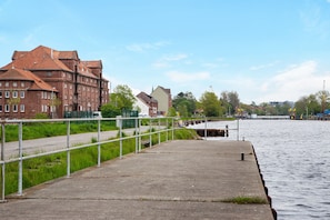 A waterfront walkway with a metal railing, a concrete path, and buildings in the background.