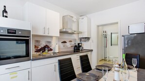 Une cuisine moderne avec des armoires blanches, un four encastré et un coin repas avec une table dressée pour deux personnes.