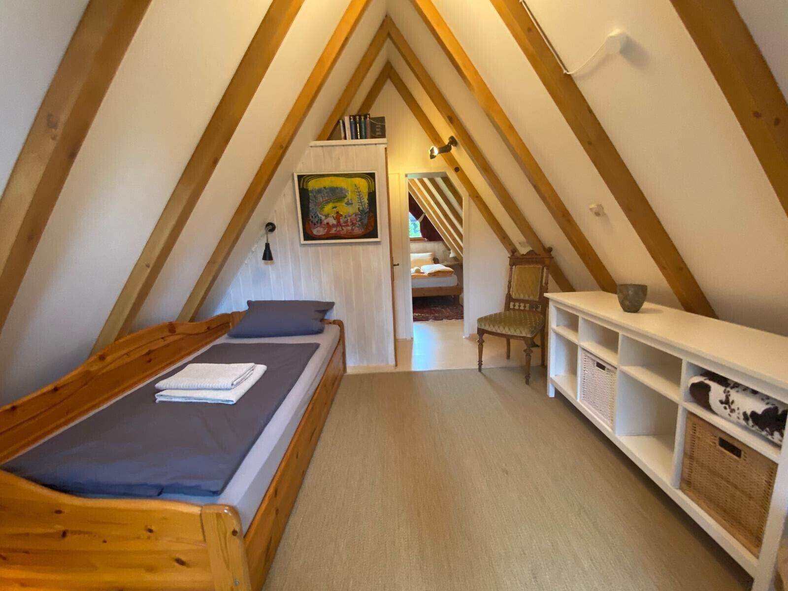 A small, cozy attic bedroom with a single bed, a chair, and a shelf unit.