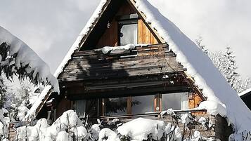 Una baita di legno con tetto spiovente, circondata da alberi imbiancati dalla neve e una recinzione in legno.