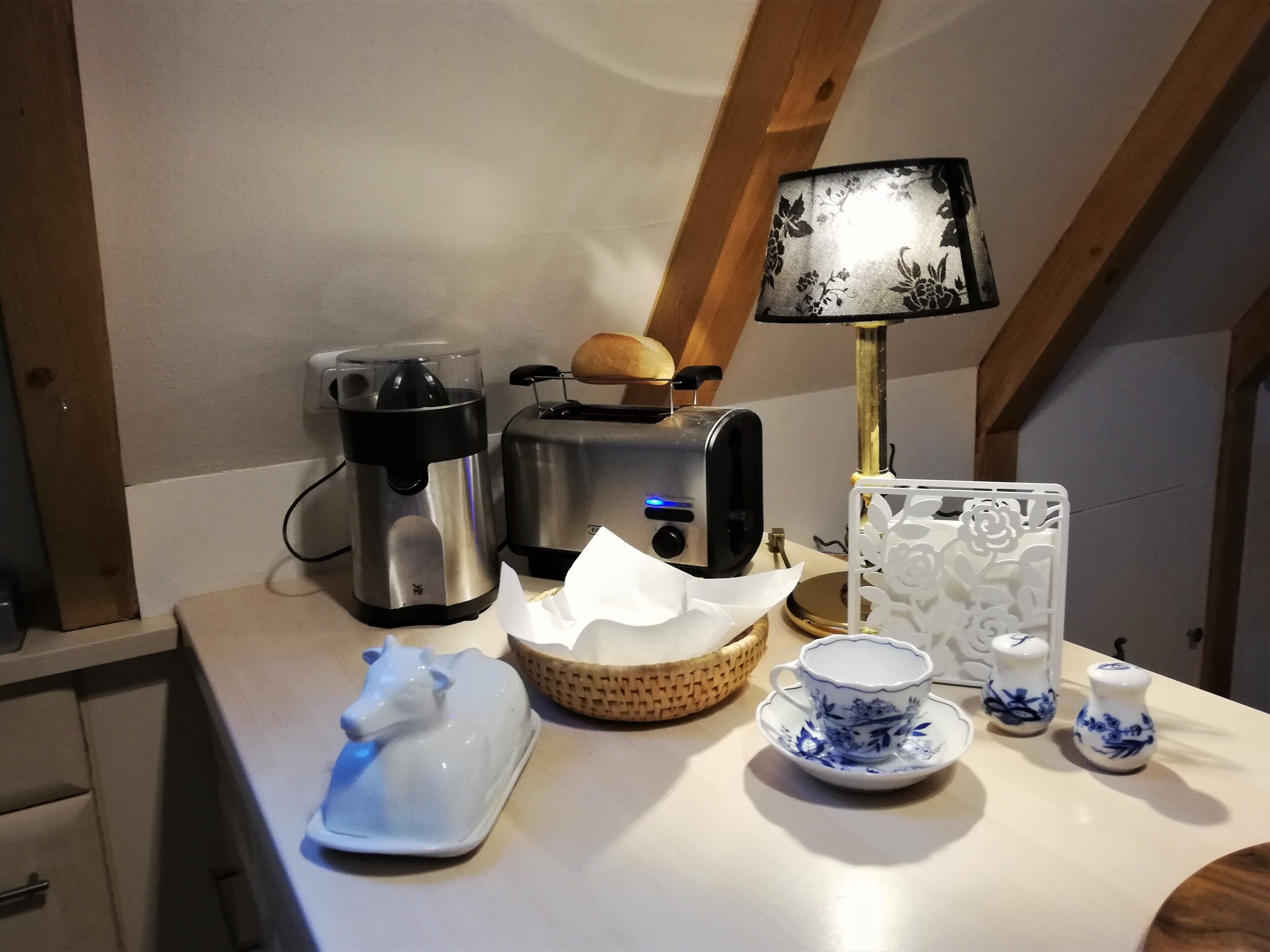 Eine Küchenarbeitsplatte mit Kaffeemaschine, Toaster, Brot, einer Lampe, einem dekorativen Teller, einer Tasse und Salzstreuern.