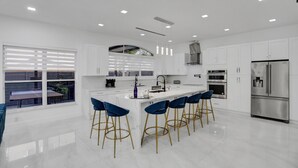 A modern kitchen with white cabinets, a stainless steel refrigerator, and bar stools. - 4 Bedroom Designer Home Next to Shul and Community Pool (Fort Lauderdale)