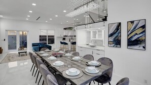 A modern dining area with a long table set for six, white cabinets, and abstract art on the walls. - 4 Bedroom Designer Home Next to Shul and Community Pool (Fort Lauderdale)