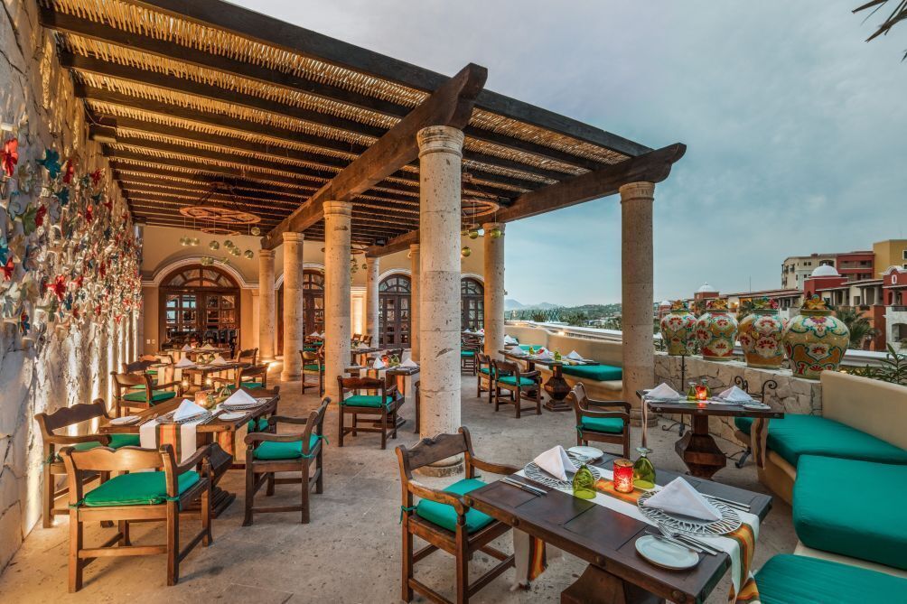 An outdoor dining area with wooden tables and chairs, a covered pergola, and decorative vases.